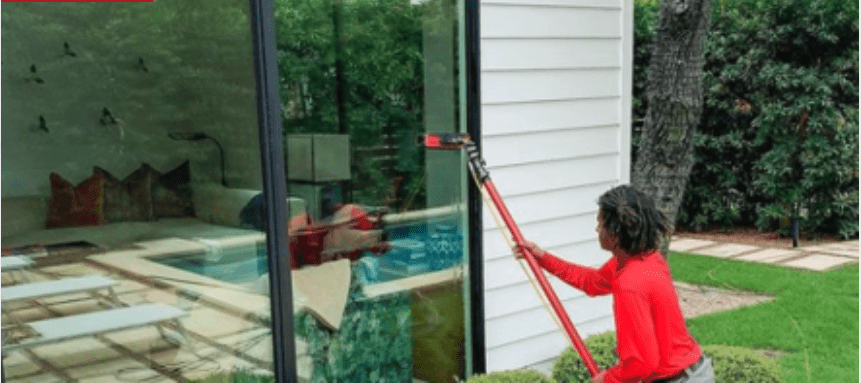 A person in a red shirt cleans a large exterior window reflecting an indoor pool. TITLE: