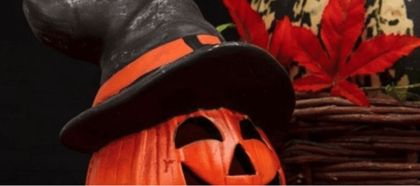 A carved orange pumpkin wearing a witch's hat sits beside a woven basket and red autumn leaf