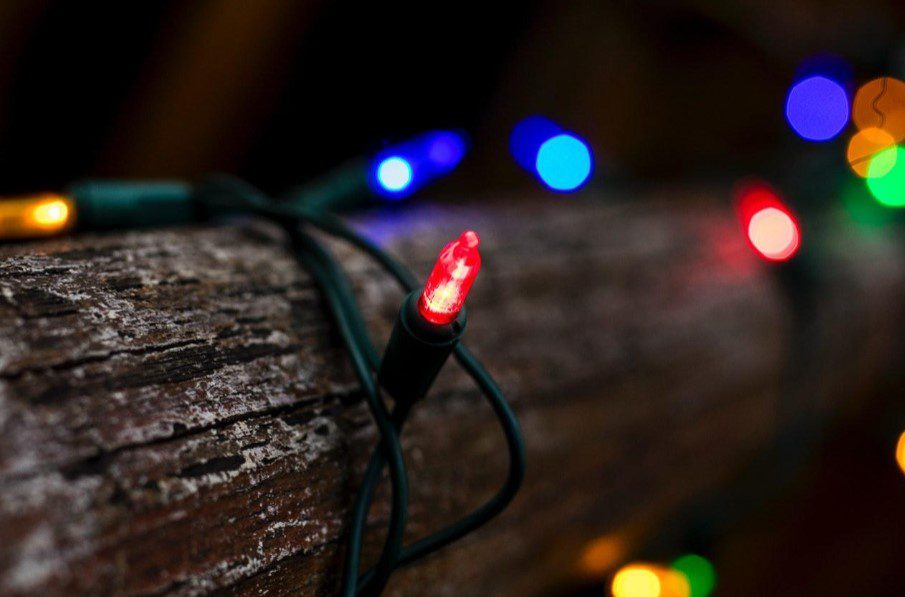 Close-up of a glowing red Christmas light on textured wood with blurred colorful lights. TITLE