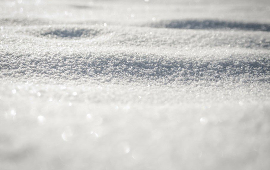 Close-up of sparkling white snow with a textured surface and soft bokeh lights.