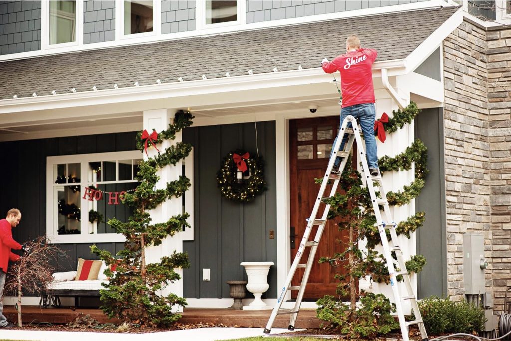 Professional decorators hang Christmas lights and garlands on a house's exterior for the holidays.