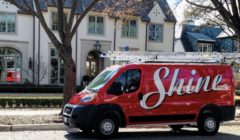 A red Shine service van with ladders is parked in front of a large, elegant house.