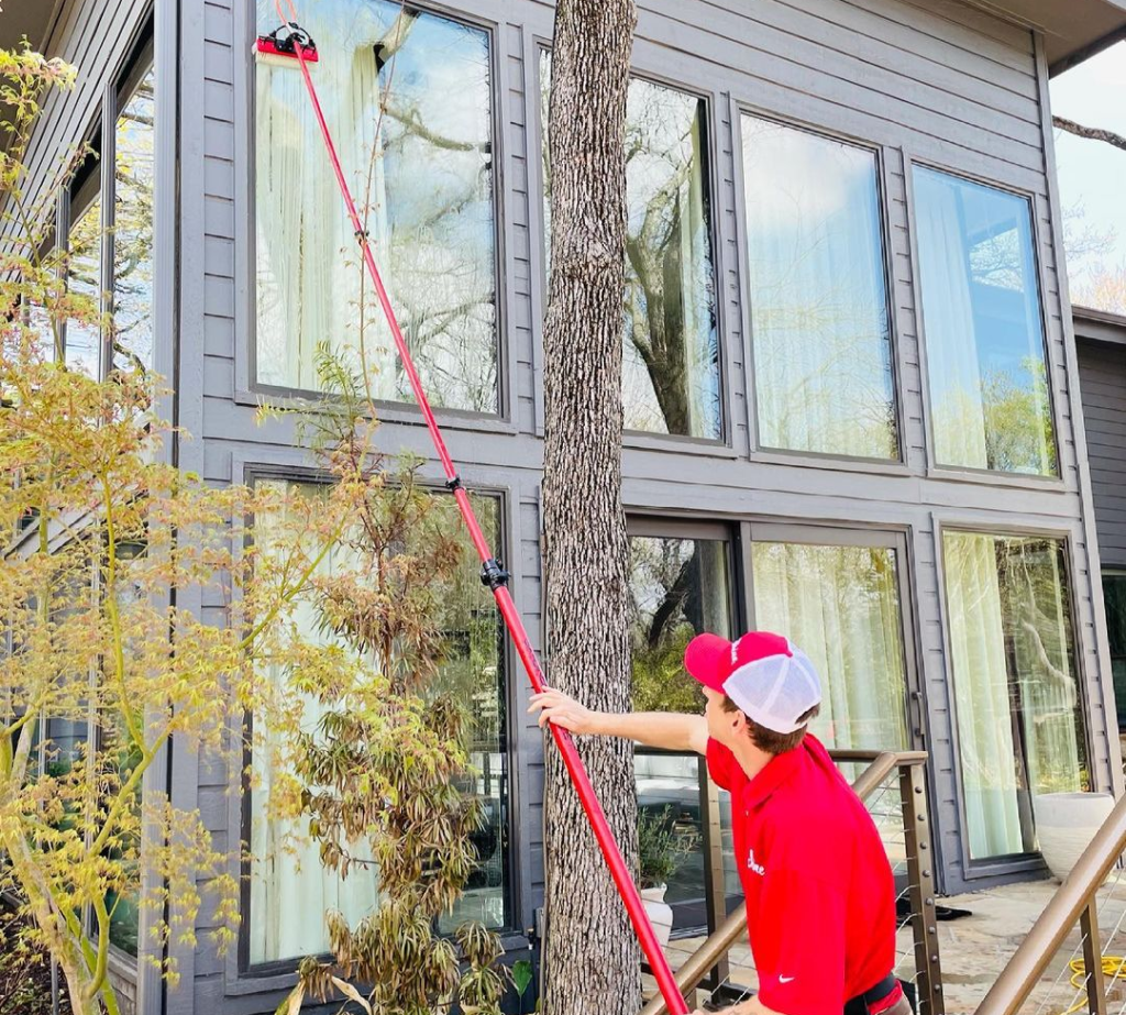 A window cleaner uses a long pole to wash high windows on a contemporary grey house. TITLE