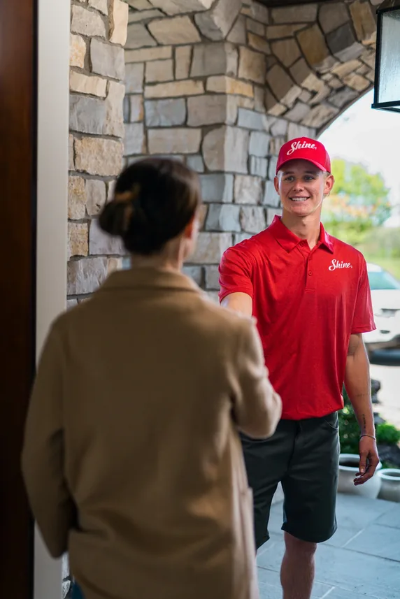 Shine technician in red uniform talking with a homeowner at a residential entrance