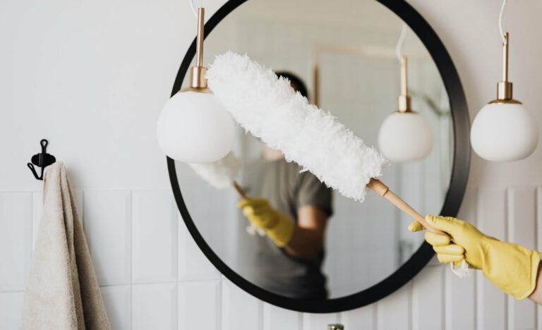 A person with a dust wand dusting lights in a bathroom.