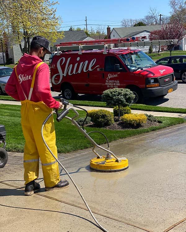 Driveway cleaning, power washing on dirty driveway in need of maintenance by Shine of Long Island technician with Shine van in the background