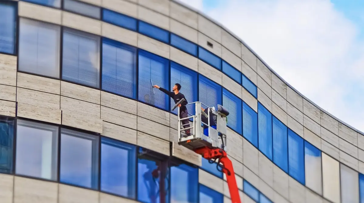 Man on a mechanical lift cleans commercial windows near the top of a building