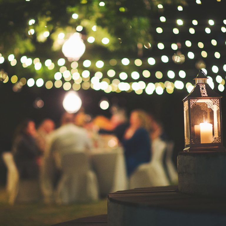 Photo with string lights over people seated at table in a group setting.