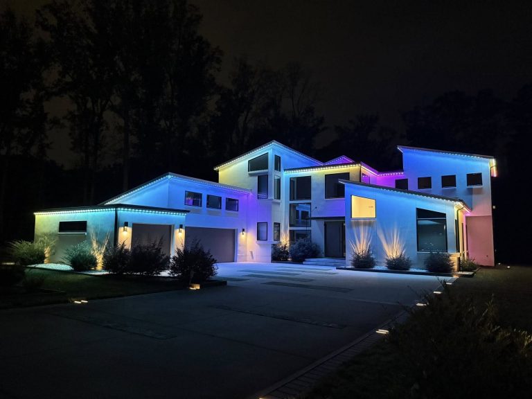 Modern home illuminated at night with colorful exterior architectural lighting.