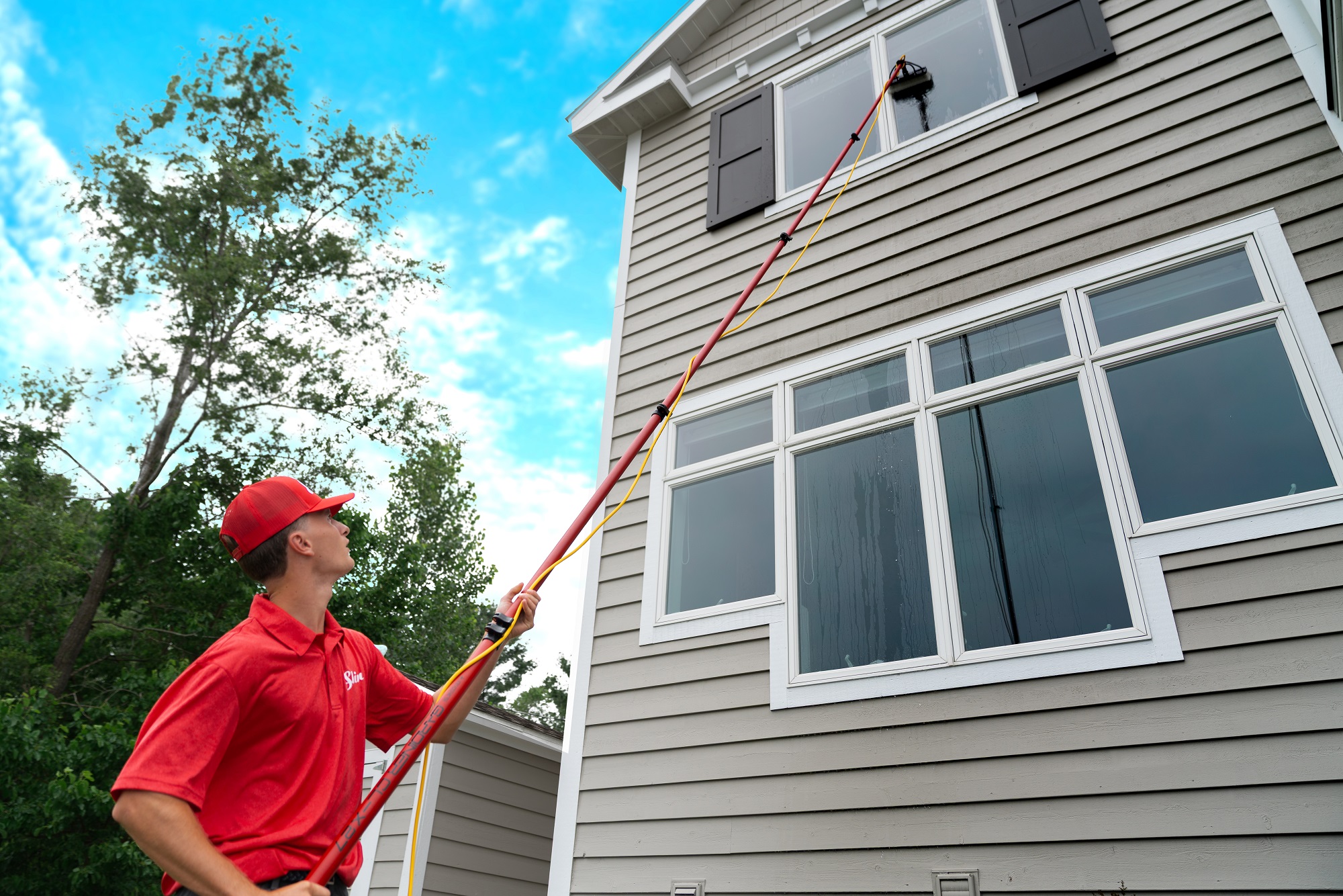 Shine technician using a water-fed pole to clean a second-story window