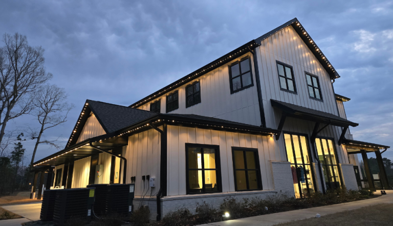 Two-story modern house illuminated at dusk with warm exterior roofline lighting.