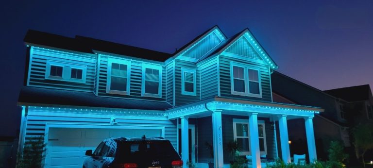 Two-story home illuminated at night with blue permanent exterior lighting along the roofline and facade.