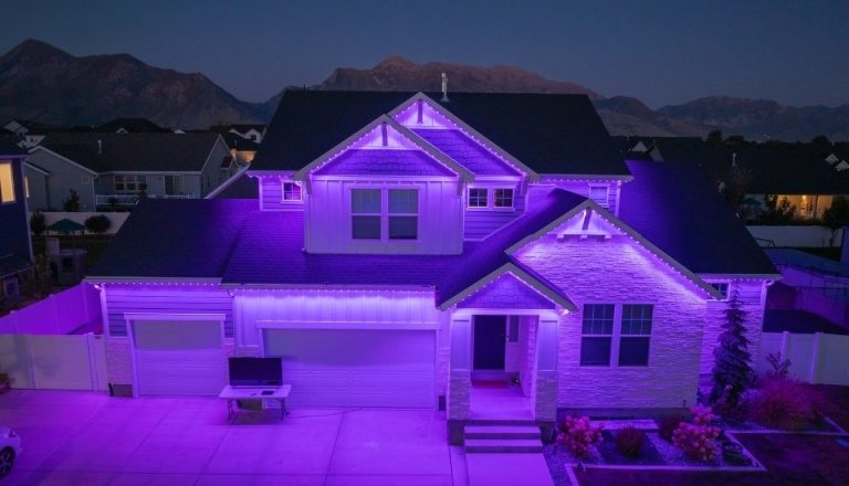 Home illuminated at night with purple permanent exterior lighting along the roofline and facade.
