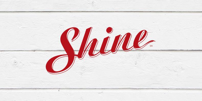 Red cursive "Shine" logo with a service mark on a textured white wood background.