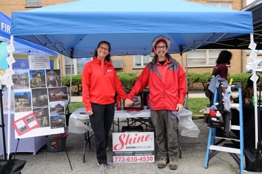 Smiling man and woman in red promote Shine window cleaning services at their outdoor booth. TITLE: