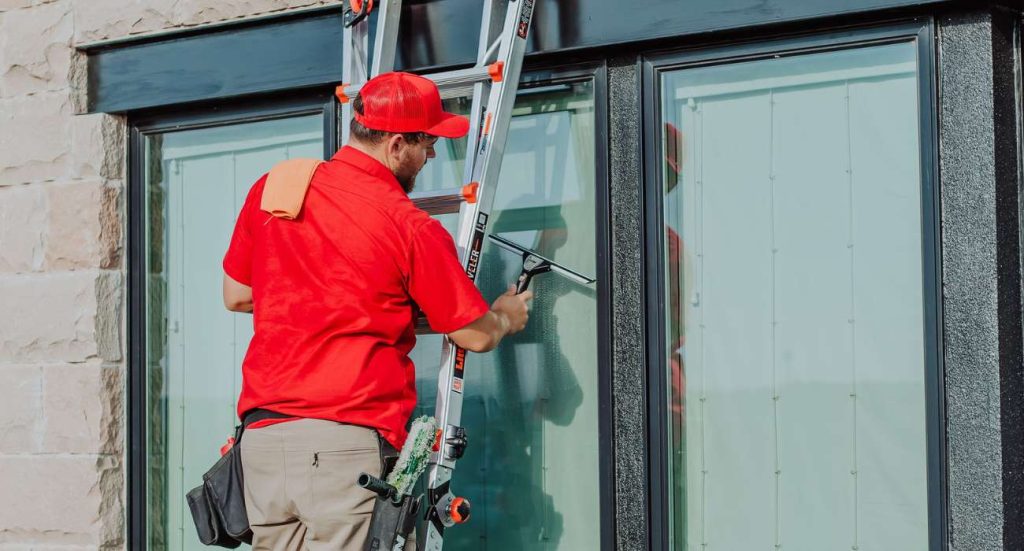 A professional window cleaner in a red uniform uses a squeegee on a large exterior