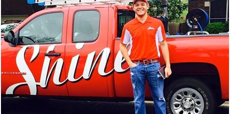 A smiling man in an orange uniform stands proudly beside a red Shine service truck. TITLE