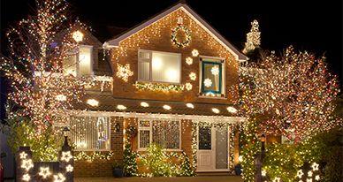 A brick house and surrounding trees are brilliantly illuminated with numerous festive Christmas lights at night.