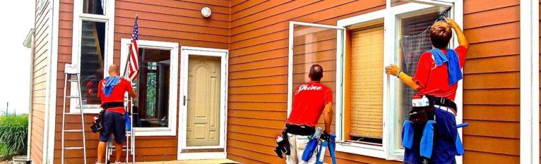 Professional window cleaners service an orange residential house with multiple windows.