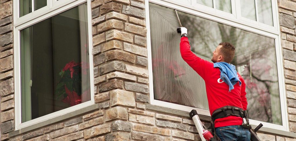 A man on a ladder cleans a building window with a squeegee, leaving soapy streaks. TITLE