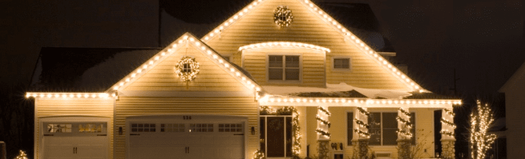 A house at night is brightly illuminated with warm white Christmas lights and decorative wreaths.